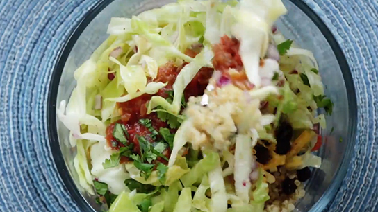 A bowl of of lettuce, tomato, cilantro and other taco stuffings mixed together. 