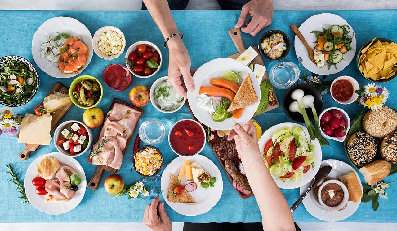 A large table full of food and hands passing a dish.