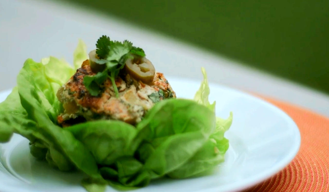 A plated chicken burger atop a bed of lettuce.