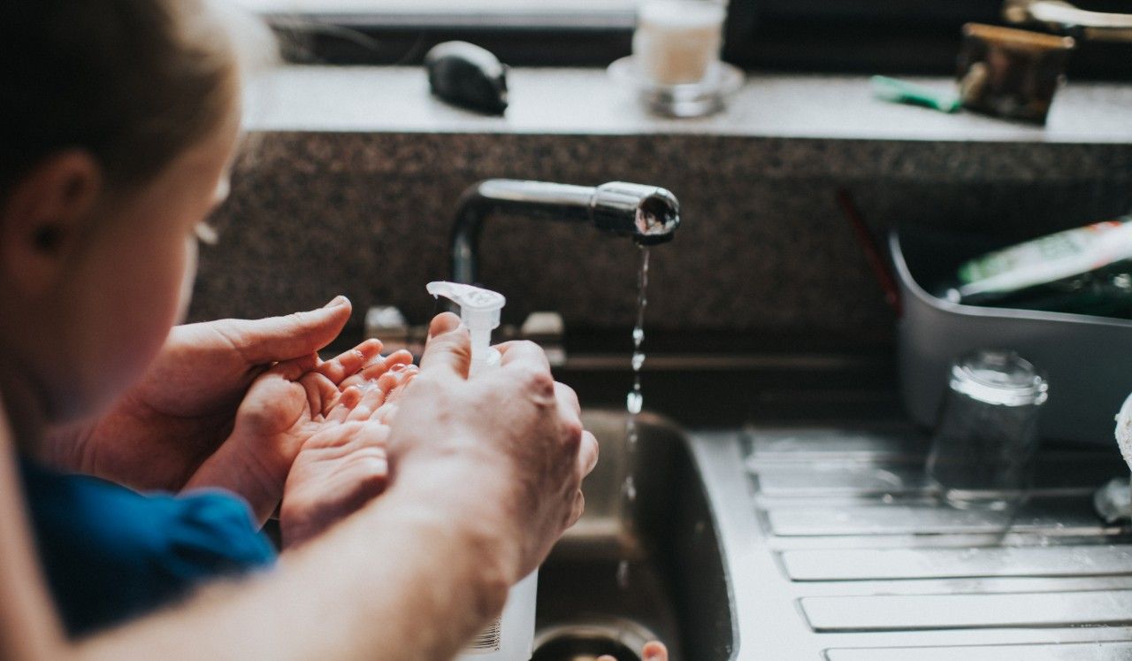 An adult and child using hand-over-hand instruction to wash hands.