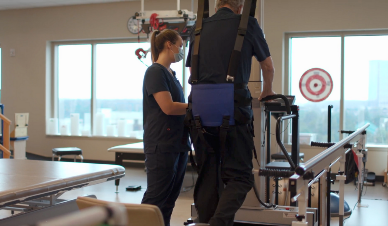 Patient recovering from COVID works with therapist and assistive equipment to  walk.