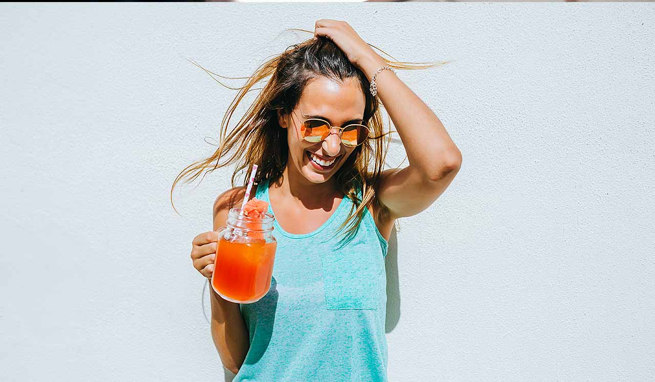 A woman holding a brightly colored drink in a glass jar.