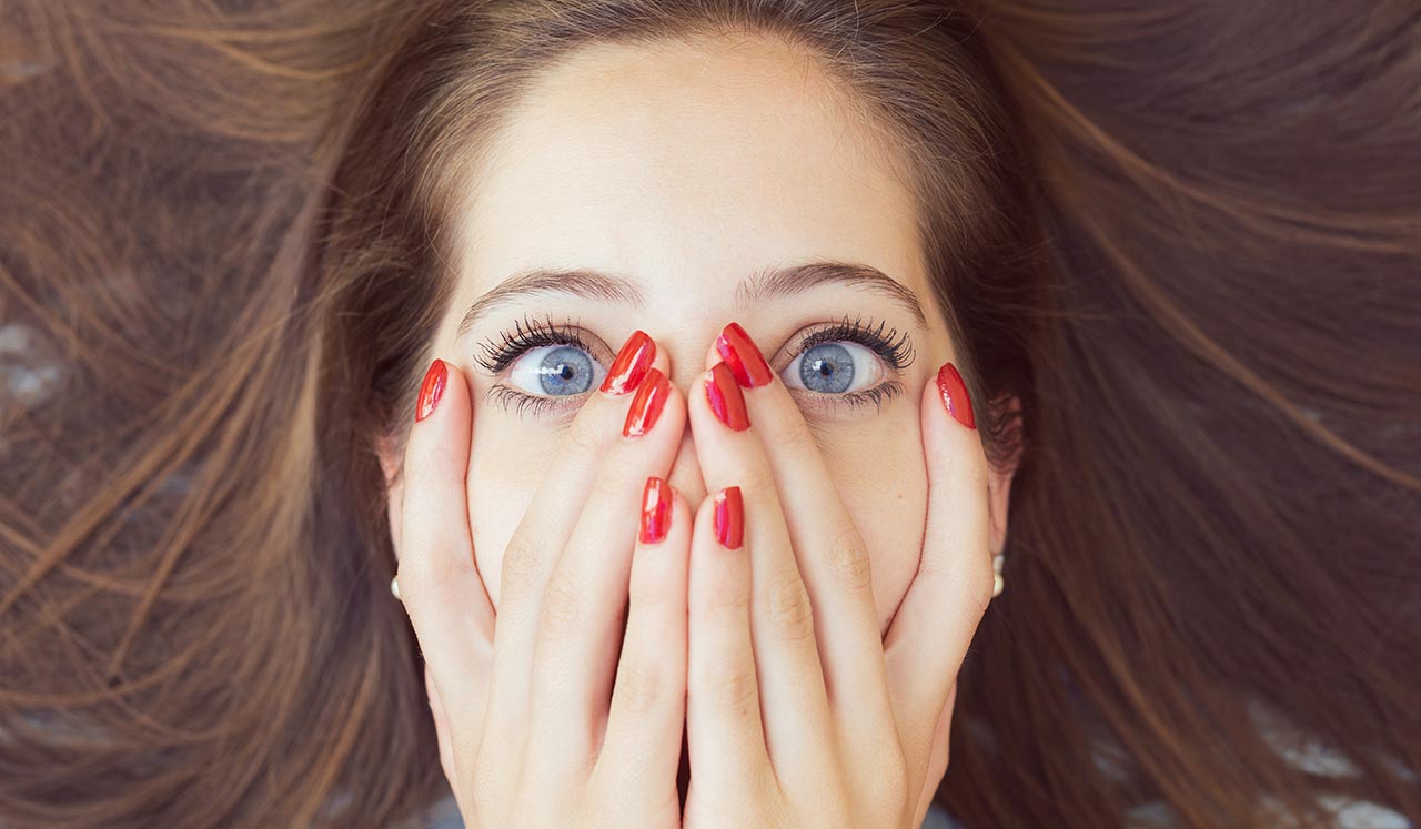 A woman with her hands over her face with red nails.