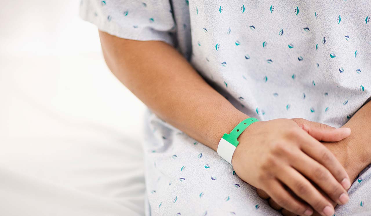 A person seated, wearing a hospital gown.