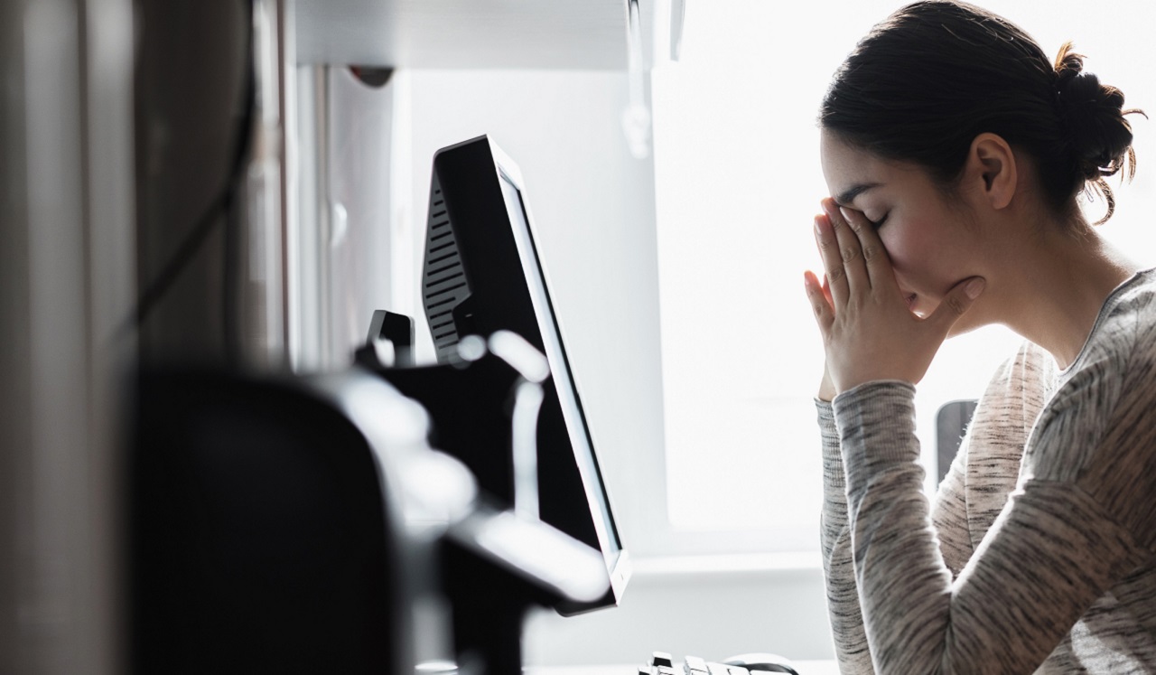 A woman holding her hands to her face at her desk.