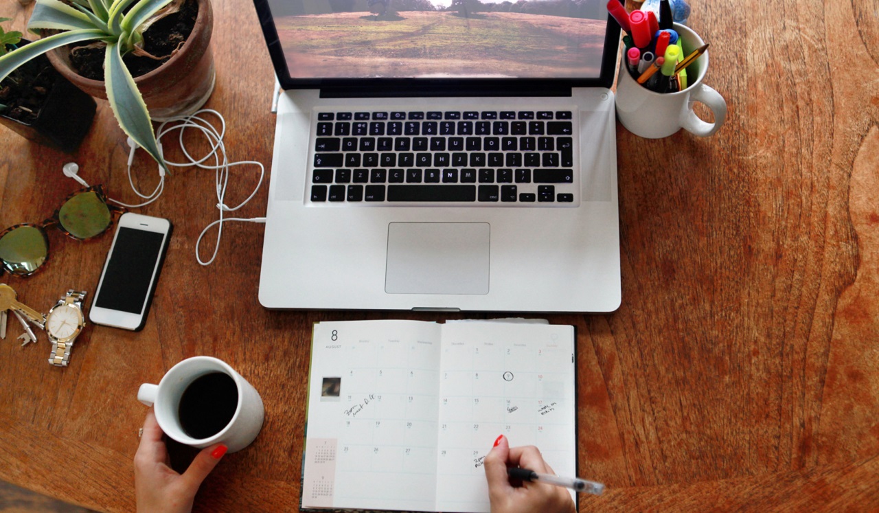 An aerial view of a desk with laptop, planner, coffee and a plant.