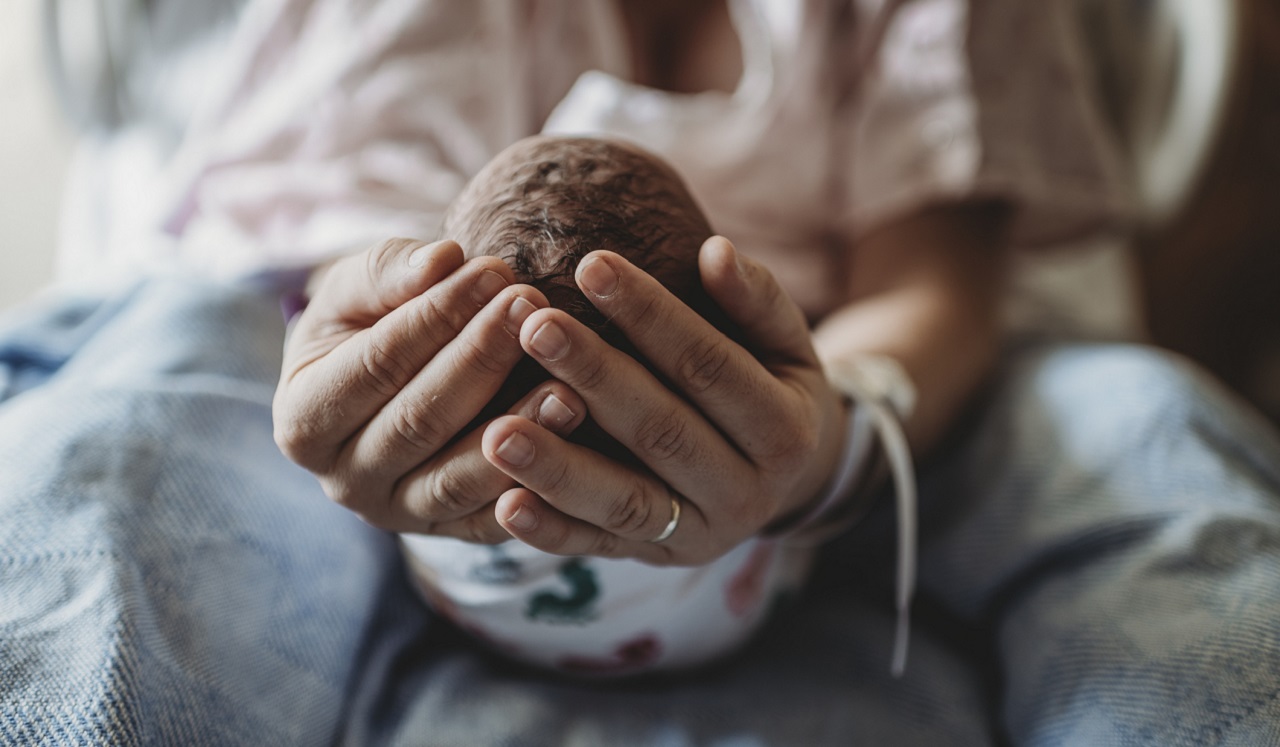 A new mother cupping her baby's head in her hands.