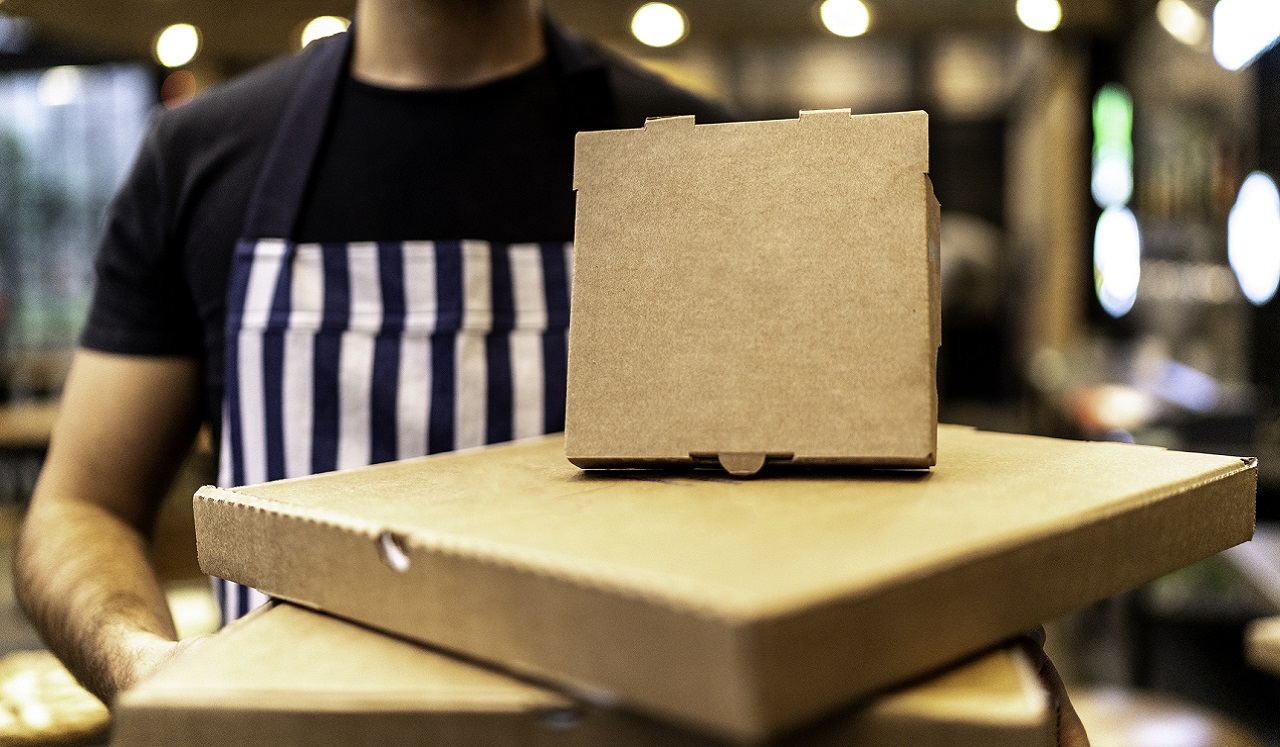 An assortment of take-out food boxes being held by a person donning a striped apron.