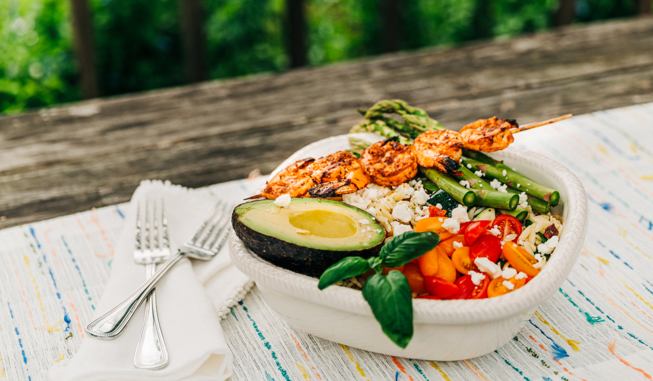 A colorful salad topped with an avocado and grilled shrimp.