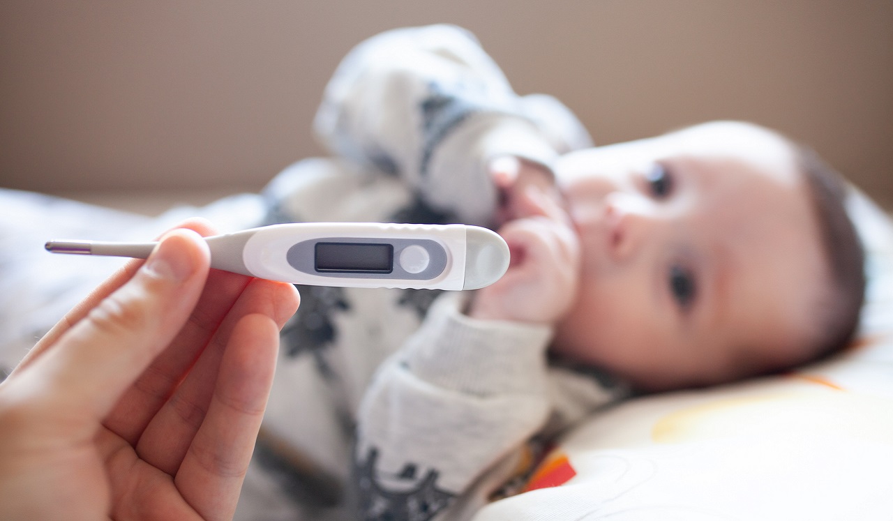 A baby sucks it's thumb following a temperature check.