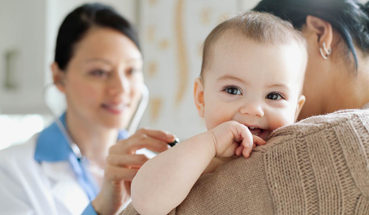 A mother holding her baby while a doctor holds a stethoscope to the baby's back.