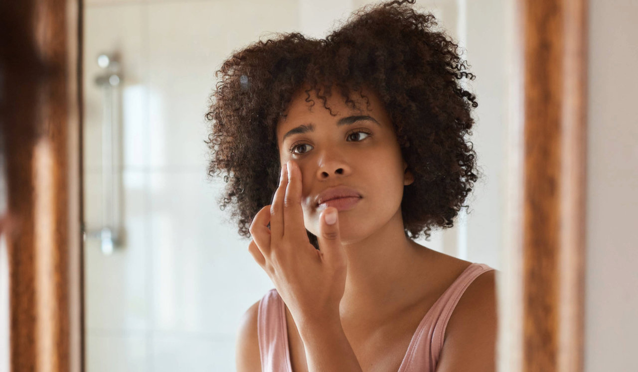 Woman looking in mirror, examining skin.