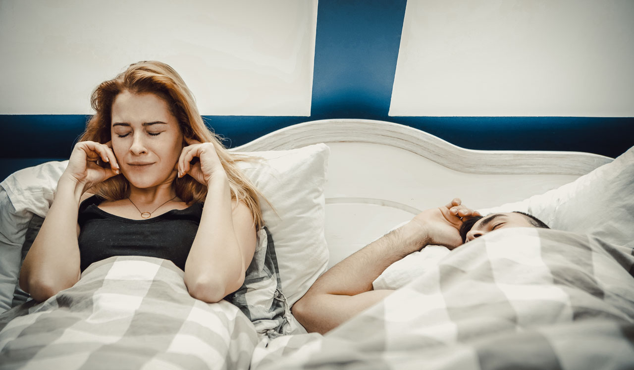 A woman holds her ears as her husband snores beside her.