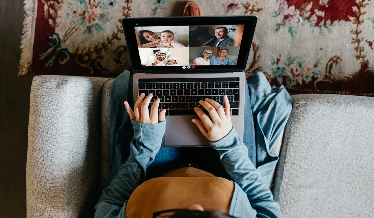 A woman holds her computer in her lap as she virtually chats with friends.