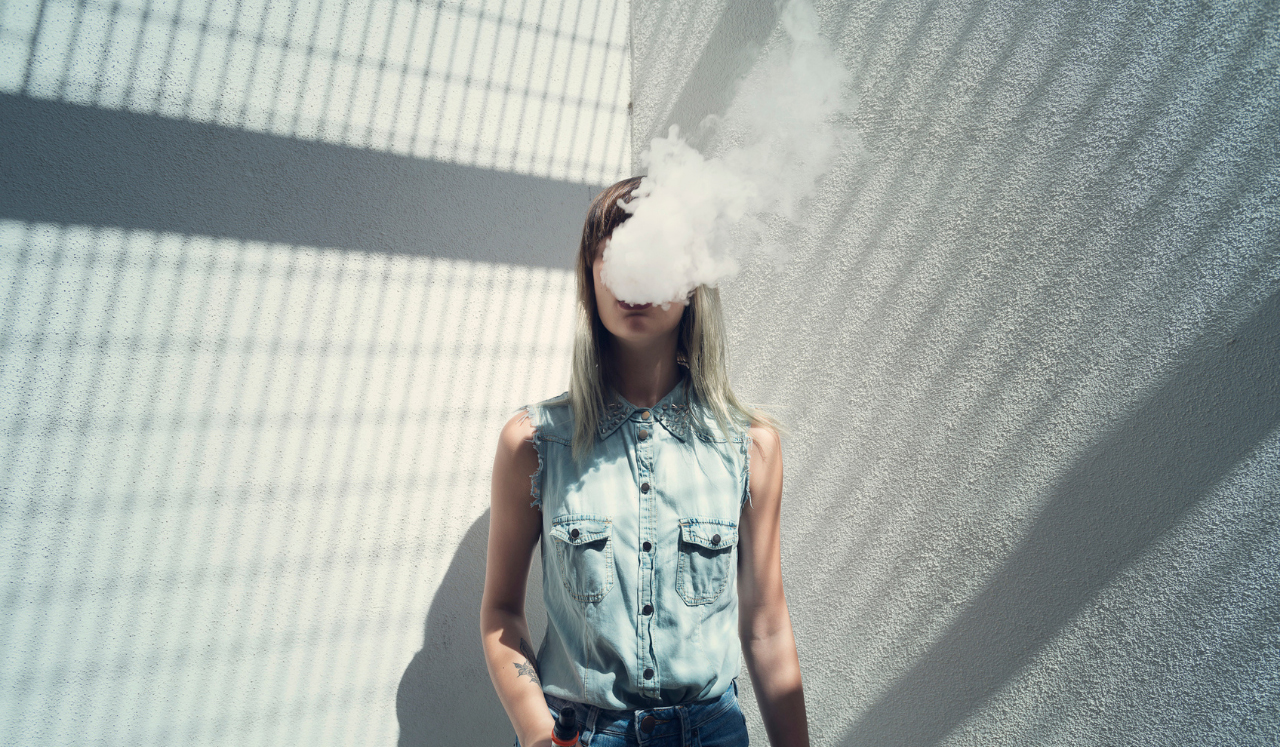 A teenage girl with smoke leaving her mouth and obscuring her face.