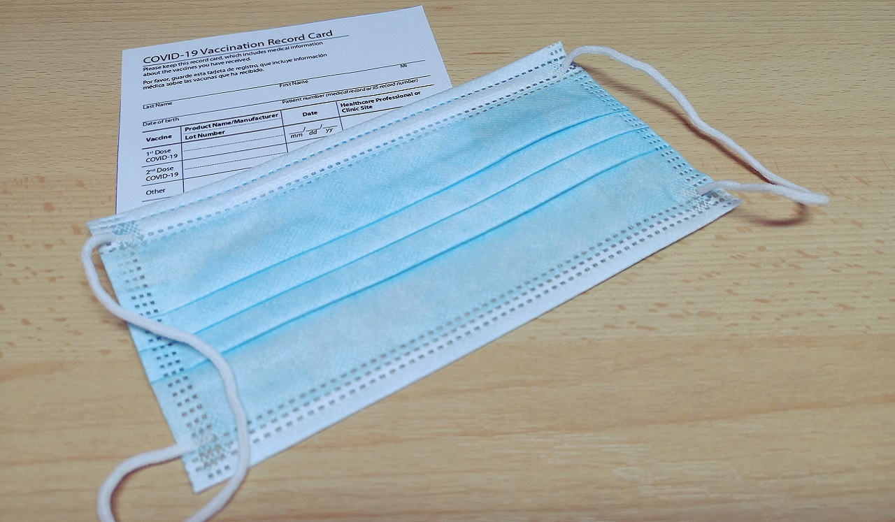 A vaccination record card and face mask on a table.