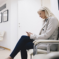 A woman looking at her phone while in the waiting area of a doctor's office.