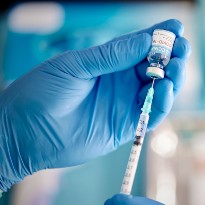 A gloved hand uses a syringe to extract medicine from a vial.