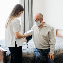 In a hospital setting, a clinician checks the blood pressure of a masked patient. 