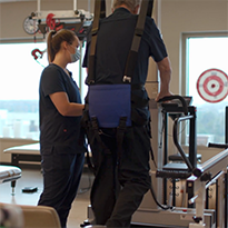 Patient recovering from COVID works with therapist and assistive equipment to  walk.