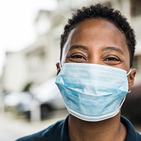 A young man is visibly smiling behind a blue medical-grade mask.