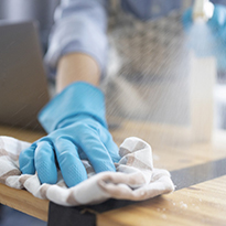 A gloved hand using a rag to wipe down a work surface.