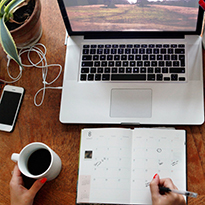 An aerial view of a desk with laptop, planner, coffee and a plant.