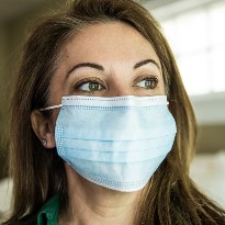 A middle-aged woman wearing a mask looks off into the distance.