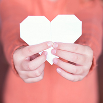 A pair of hands holds up a paper heart.