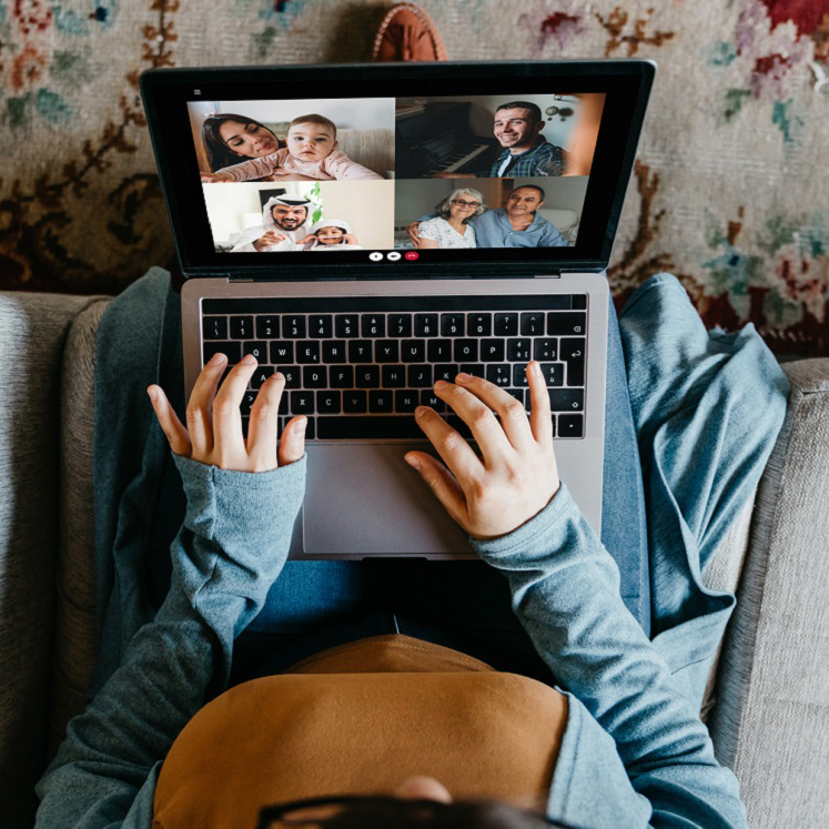 A woman holds her computer in her lap as she virtually chats with friends.