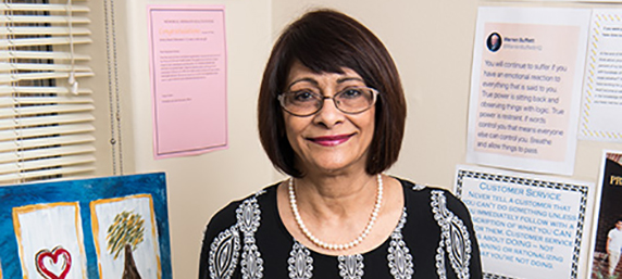 Faizbano Rayani smiles, standing by her work desk adorned with letters and pictures.