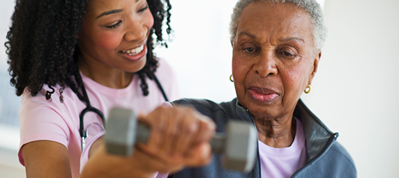 A home health professional helps a woman while lifting a hand weight.