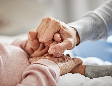 An elderly pair of hands being held earnestly by another's hands.