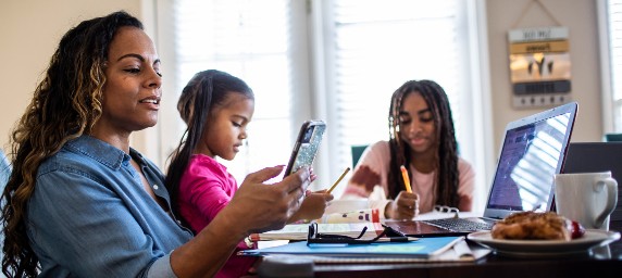 A mother and her two daughters are gathered round the dining table working on different activities.