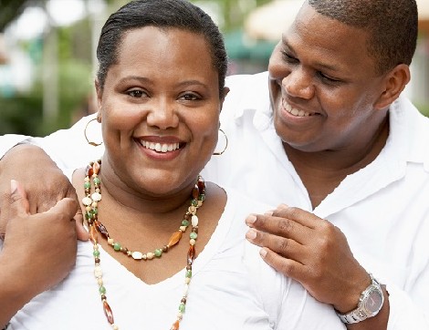 A woman smiles for the camera, as her husband looks at her adoringly.