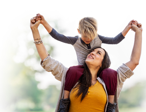 A woman smiles, looking up at her son on her shoulders.