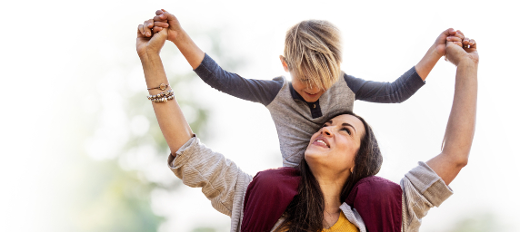 A woman smiles, looking up at her son on her shoulders.