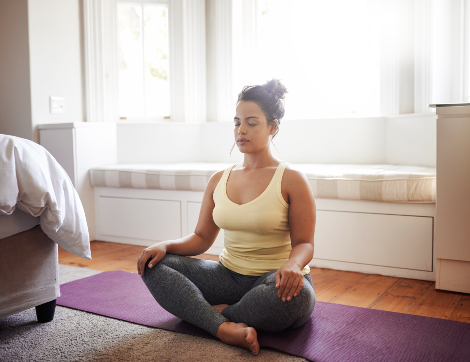 A young woman meditates in her bedroom.