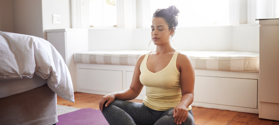 A young woman meditates in her bedroom.