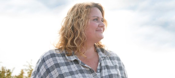 A woman in a plaid shirt smiles as she looks off into the distance of the great outdoors.