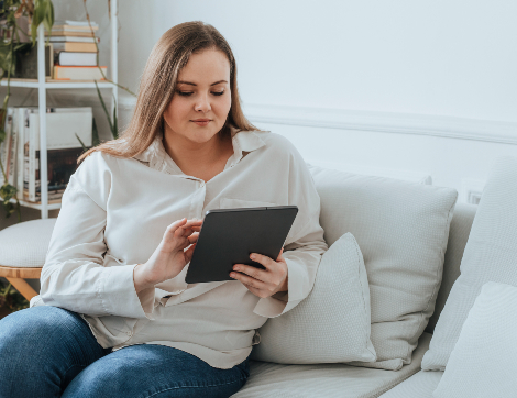 A young woman interacts with a tablet from her couch.