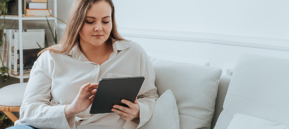 A young woman interacts with a tablet from her couch.