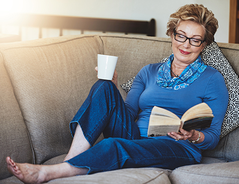 A woman reclines while enjoying a book on the couch