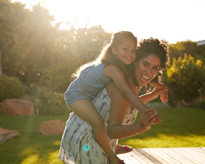 Woman and daughter smile while mother gives a biggie-back ride.